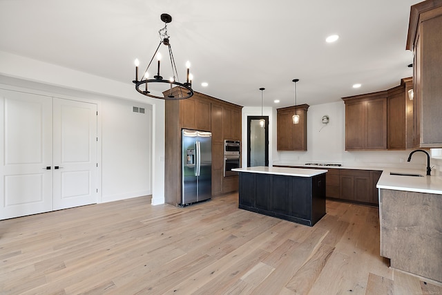 kitchen with pendant lighting, appliances with stainless steel finishes, a kitchen island, sink, and a chandelier