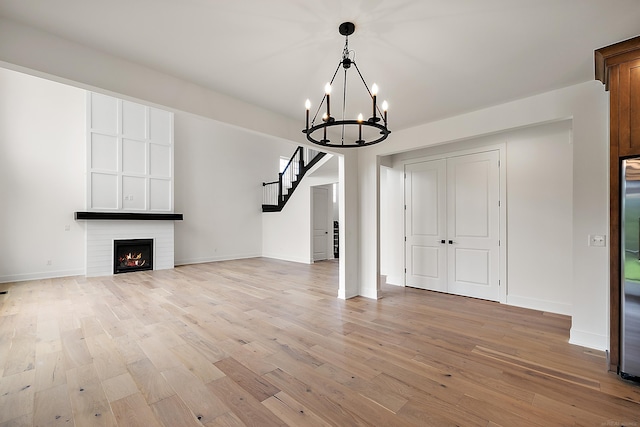 unfurnished living room with a fireplace, light wood-type flooring, and a notable chandelier