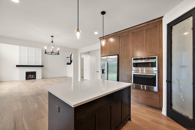 kitchen featuring pendant lighting, appliances with stainless steel finishes, a center island, a fireplace, and a notable chandelier