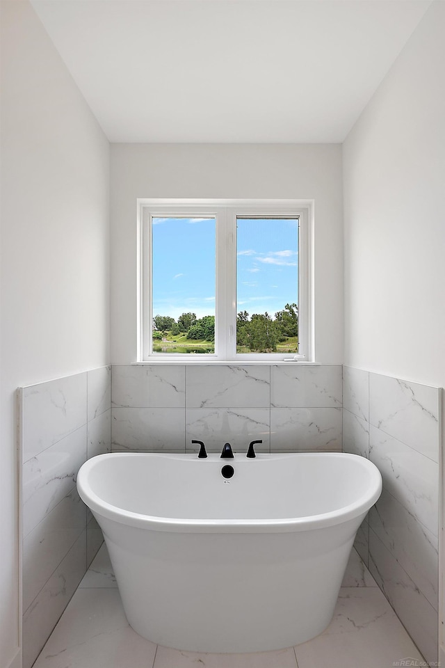 bathroom featuring a bath, a wealth of natural light, and tile walls