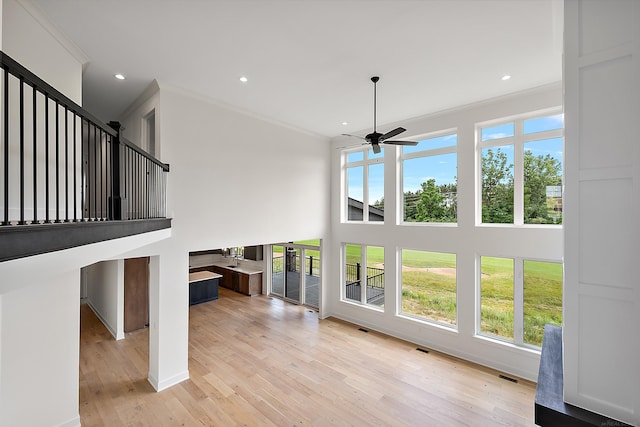 unfurnished living room featuring crown molding, light hardwood / wood-style floors, ceiling fan, and a wealth of natural light