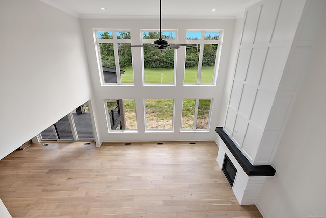 unfurnished living room with ceiling fan, crown molding, and light wood-type flooring