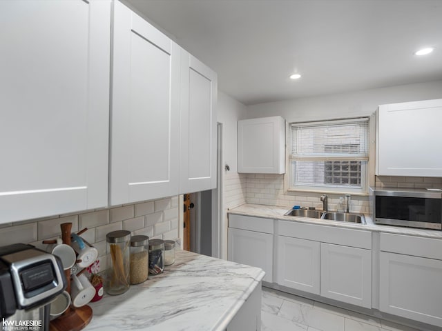 kitchen with white cabinets, decorative backsplash, light stone countertops, and sink