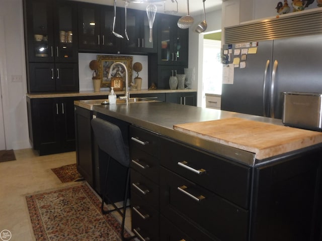 kitchen featuring a kitchen island with sink, light tile patterned floors, hanging light fixtures, and stainless steel built in refrigerator