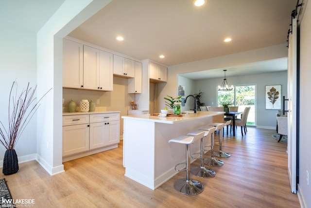 kitchen featuring pendant lighting, white cabinets, a kitchen island with sink, light hardwood / wood-style floors, and a barn door