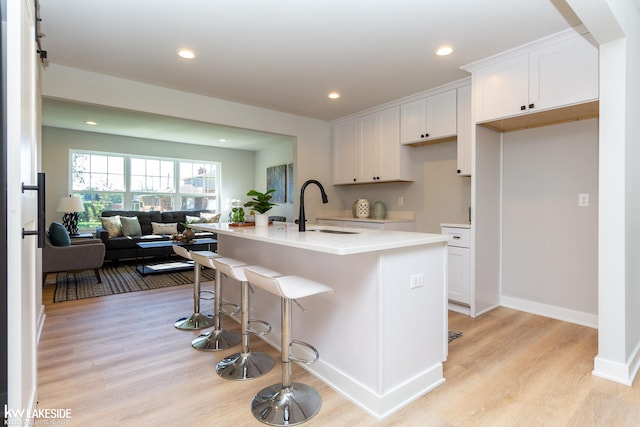 kitchen with white cabinetry, sink, light hardwood / wood-style floors, and an island with sink