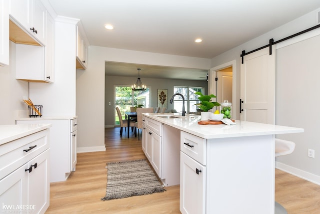 kitchen featuring an island with sink, a barn door, sink, and white cabinets