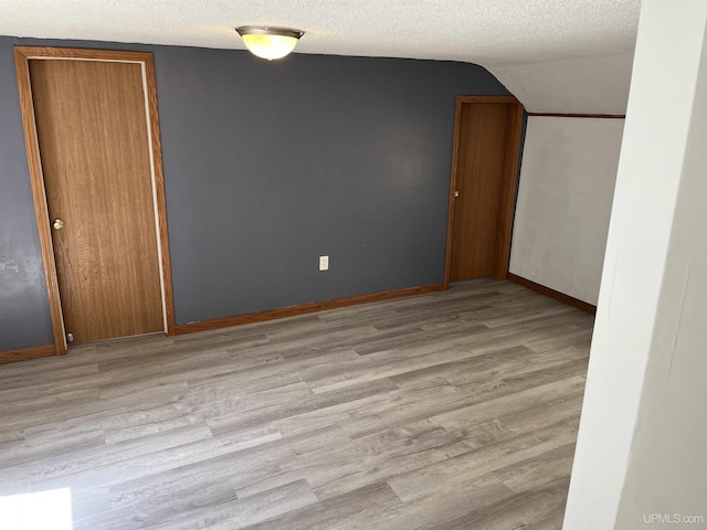 empty room with light wood-type flooring, a textured ceiling, and vaulted ceiling