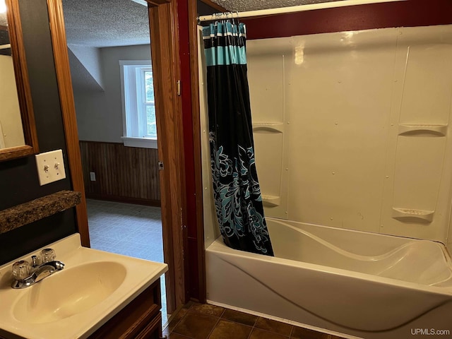 bathroom featuring vanity, a textured ceiling, shower / bath combo with shower curtain, and wood walls