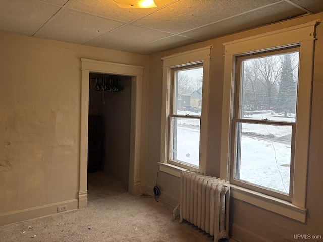 spare room featuring a paneled ceiling, radiator heating unit, and light colored carpet