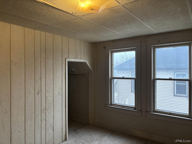 unfurnished bedroom with a paneled ceiling, wood walls, and a closet