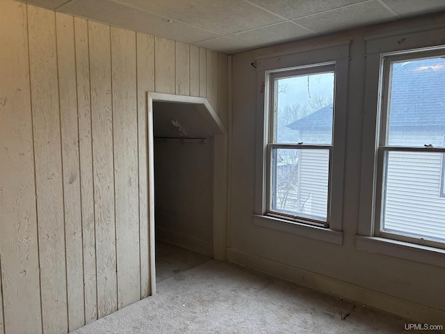 unfurnished bedroom with multiple windows, wooden walls, and a closet