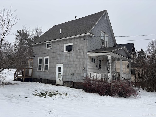 snow covered back of property featuring covered porch