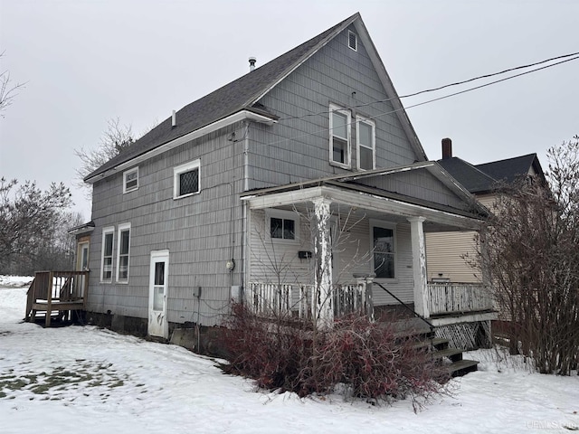 snow covered rear of property featuring covered porch