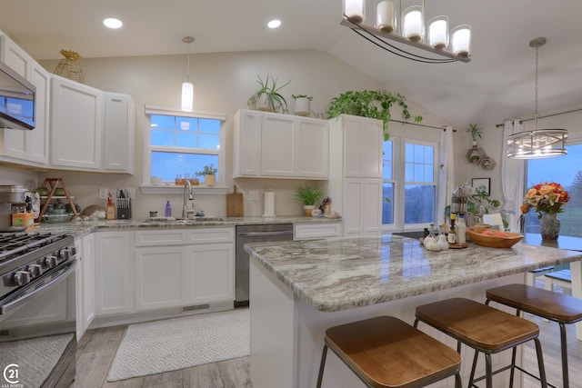 kitchen featuring a center island, vaulted ceiling, decorative light fixtures, white cabinetry, and stainless steel appliances