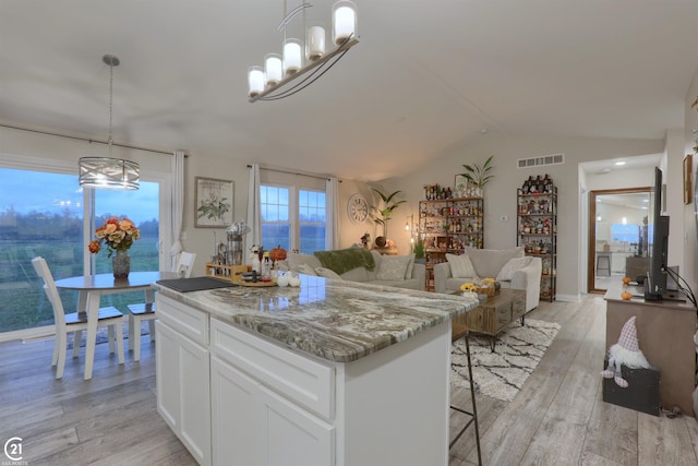 kitchen with a center island, hanging light fixtures, light hardwood / wood-style flooring, light stone countertops, and white cabinetry