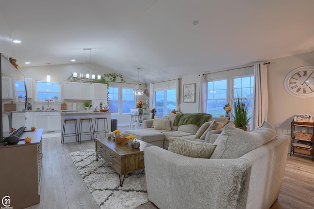 living room with a chandelier, light wood-type flooring, vaulted ceiling, and sink