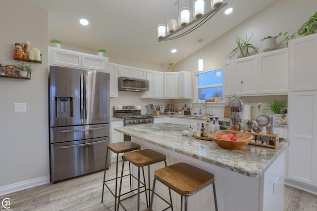 kitchen with appliances with stainless steel finishes, light wood-type flooring, light stone counters, white cabinetry, and hanging light fixtures