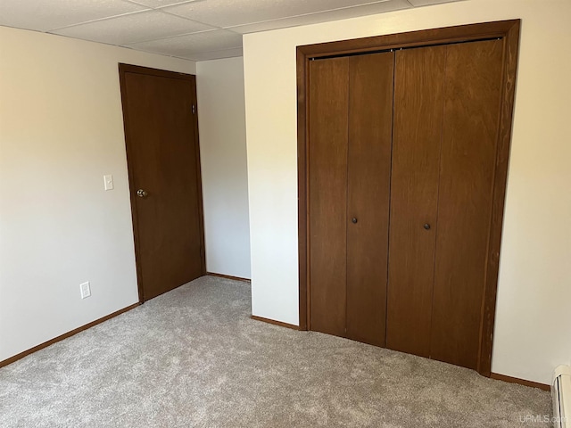 unfurnished bedroom featuring light colored carpet, a closet, and a baseboard heating unit