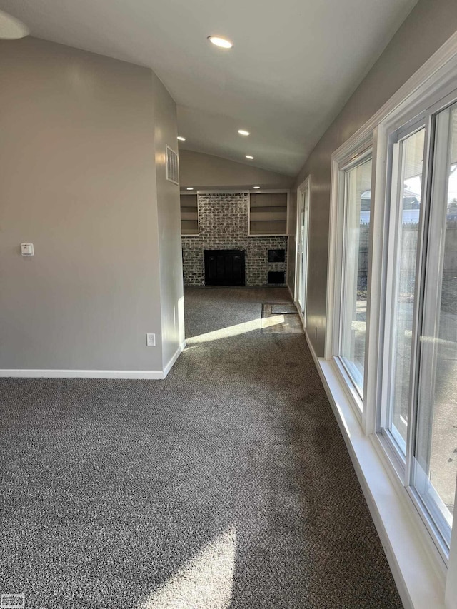 unfurnished living room with a wealth of natural light, a fireplace, lofted ceiling, and dark colored carpet