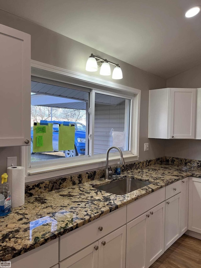 kitchen with dark stone countertops, white cabinetry, sink, and light hardwood / wood-style flooring