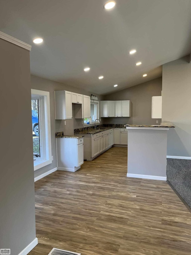 kitchen with kitchen peninsula, sink, wood-type flooring, white cabinets, and lofted ceiling