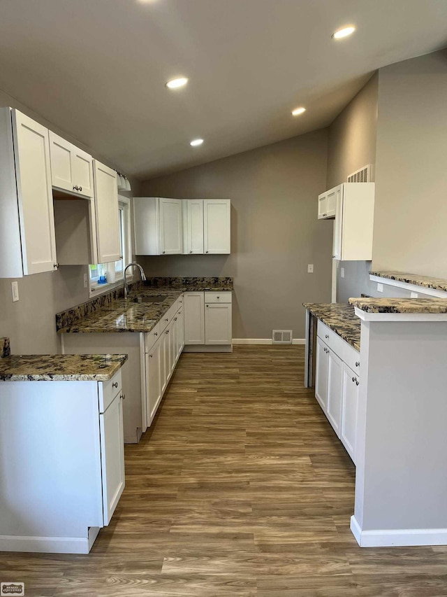 kitchen featuring white cabinets, light hardwood / wood-style flooring, vaulted ceiling, and dark stone countertops