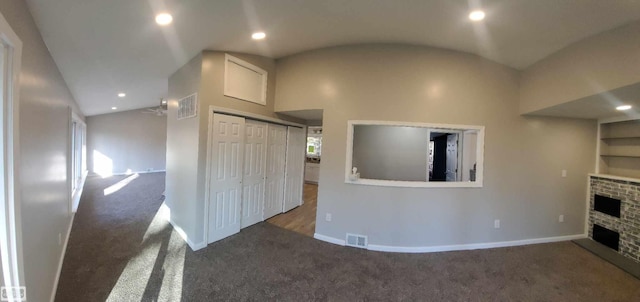 unfurnished living room featuring dark colored carpet, built in shelves, lofted ceiling, and a fireplace