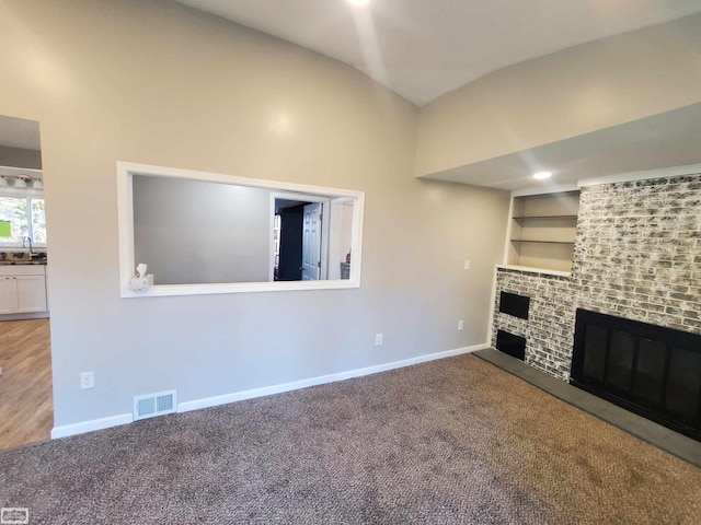 unfurnished living room with sink, built in features, carpet floors, and a brick fireplace