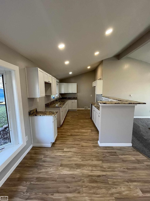 kitchen featuring sink, vaulted ceiling with beams, kitchen peninsula, wood-type flooring, and white cabinets