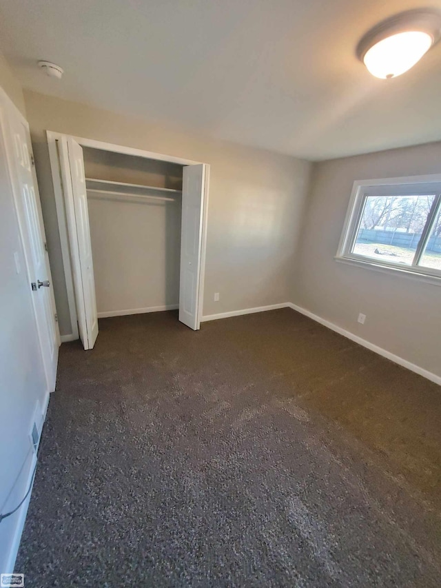 unfurnished bedroom with dark colored carpet and a closet