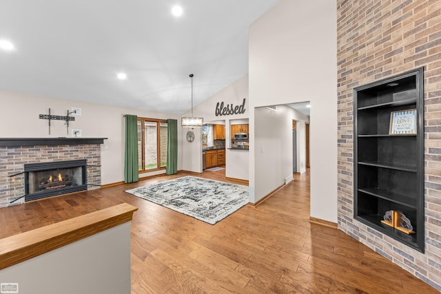 living room with built in features, light hardwood / wood-style floors, vaulted ceiling, and a brick fireplace