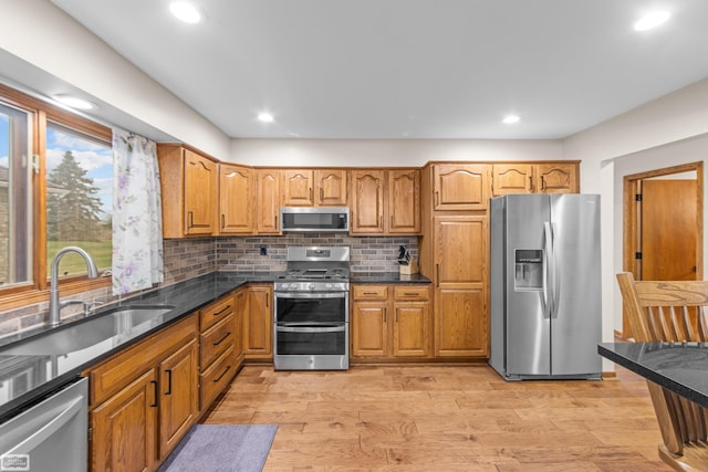 kitchen with sink, stainless steel appliances, tasteful backsplash, dark stone counters, and light hardwood / wood-style floors