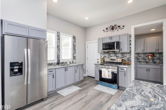 kitchen featuring light stone countertops, backsplash, stainless steel appliances, light hardwood / wood-style flooring, and gray cabinets