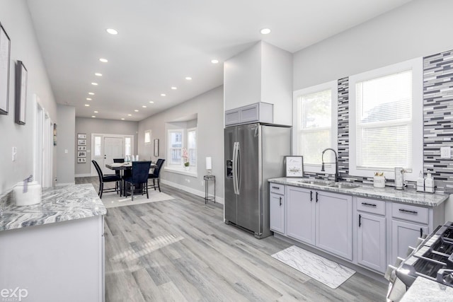 kitchen featuring light stone countertops, stainless steel fridge, gray cabinetry, sink, and light hardwood / wood-style floors