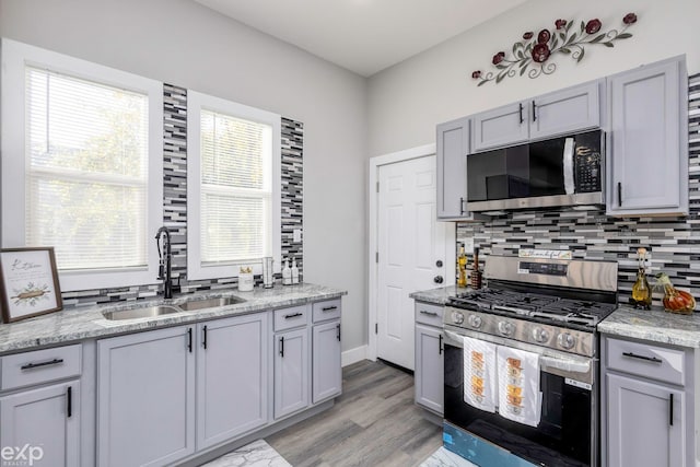 kitchen featuring gray cabinetry, light stone countertops, sink, stainless steel appliances, and decorative backsplash