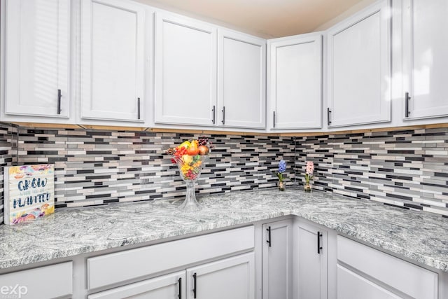 kitchen featuring backsplash, white cabinetry, and light stone counters