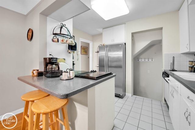 kitchen featuring a kitchen breakfast bar, decorative backsplash, stainless steel fridge, light tile patterned floors, and white cabinetry