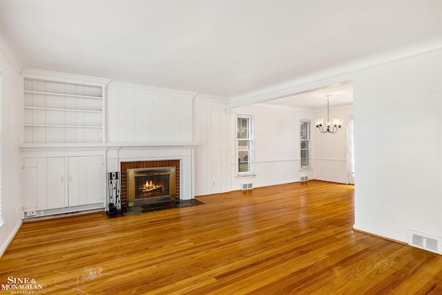 unfurnished living room with hardwood / wood-style floors, an inviting chandelier, a brick fireplace, and crown molding