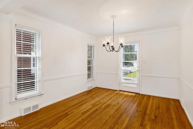 unfurnished dining area featuring hardwood / wood-style floors, crown molding, and a chandelier