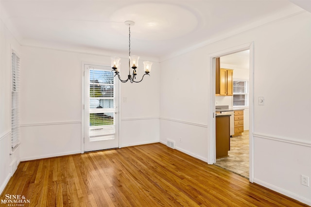 unfurnished dining area with crown molding, hardwood / wood-style floors, and an inviting chandelier