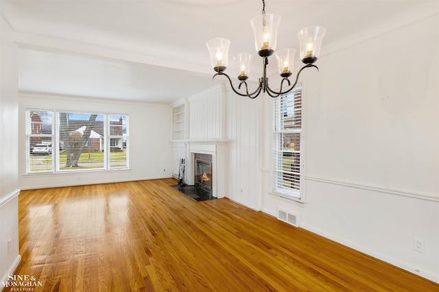 unfurnished living room featuring ornamental molding, plenty of natural light, wood-type flooring, and an inviting chandelier