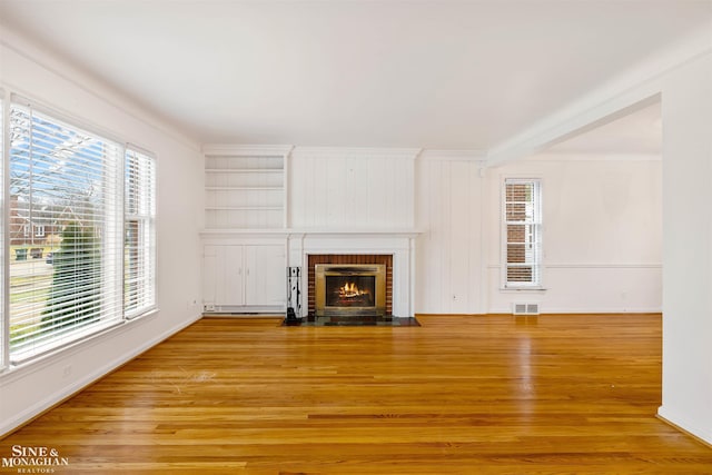 unfurnished living room featuring wood-type flooring, ornamental molding, and a brick fireplace