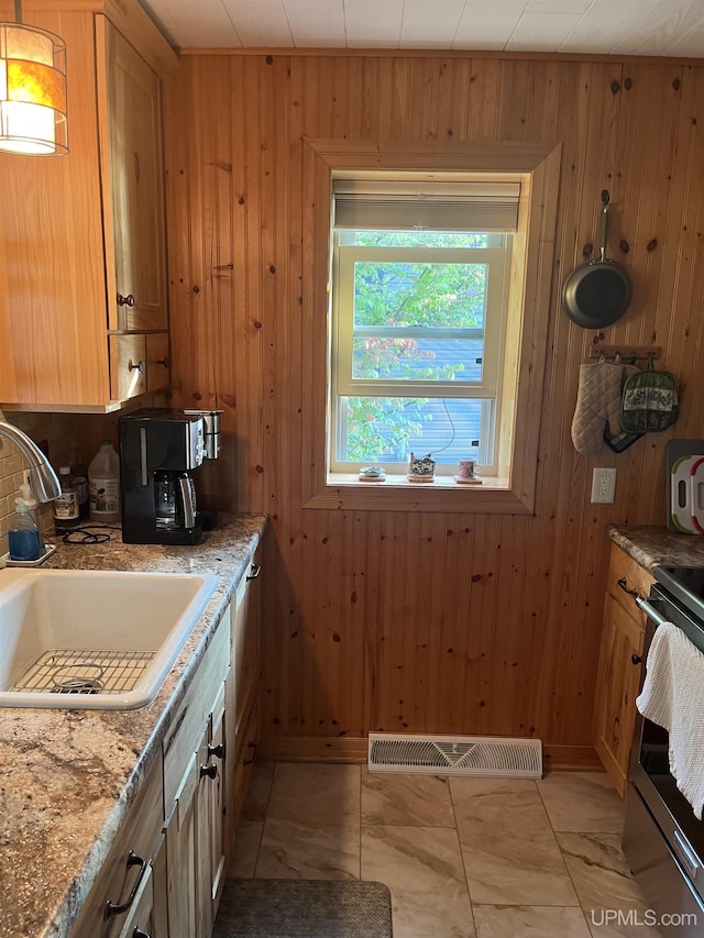 kitchen with stainless steel range with electric stovetop, wood walls, sink, light tile patterned floors, and light stone counters