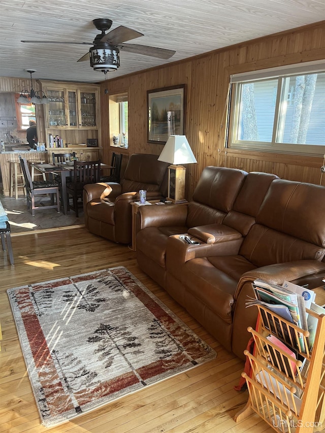 living room featuring wood-type flooring, a wealth of natural light, ceiling fan, and wooden walls