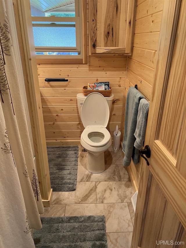 bathroom with tile patterned floors, wooden walls, and toilet