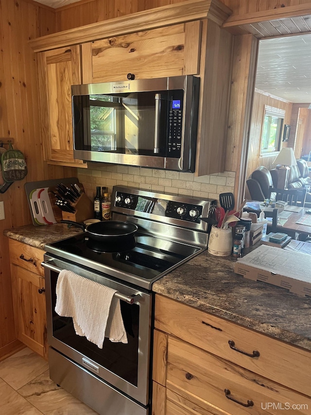 kitchen featuring stainless steel appliances, wooden walls, and dark stone counters