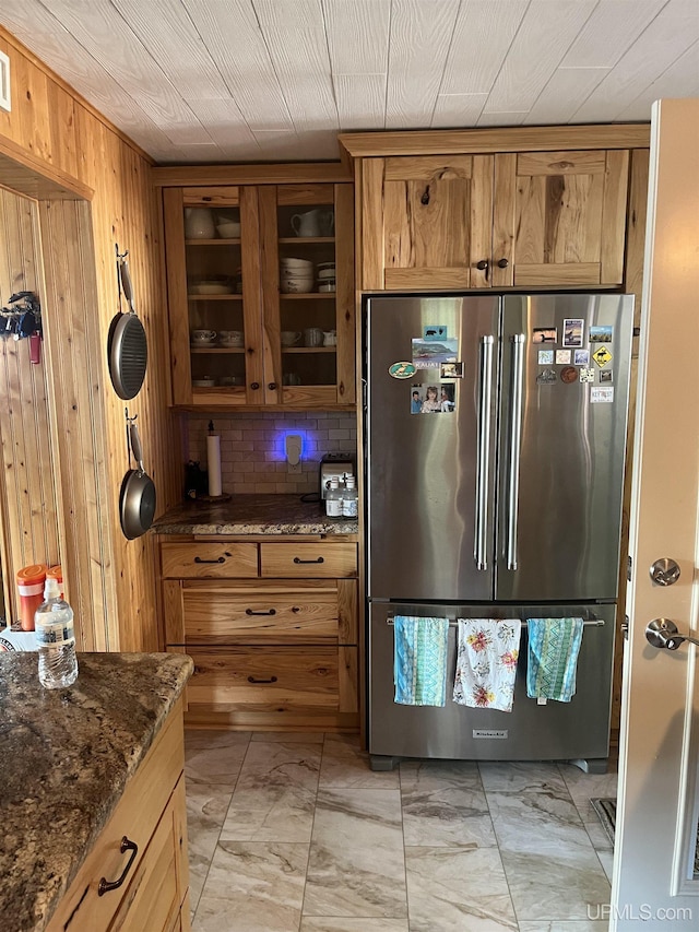 kitchen featuring backsplash, stainless steel refrigerator, wood walls, and dark stone countertops