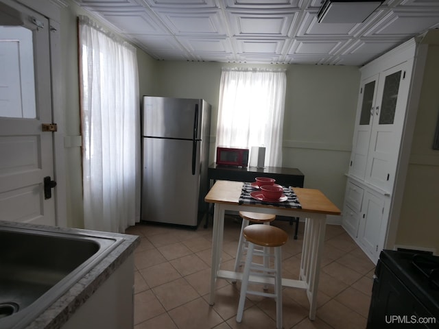 kitchen featuring stainless steel refrigerator, sink, white cabinets, and light tile patterned floors