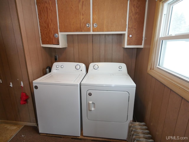 laundry area with a wealth of natural light, cabinets, wooden walls, and washing machine and clothes dryer